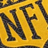 Close-up of the embroidered NFL logo, highlighting the intricate yellow stitching on a black background with geometric patterns.